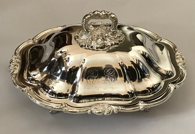 Color photograph, silver, covered casserole dish with scalloped edges and top handle.