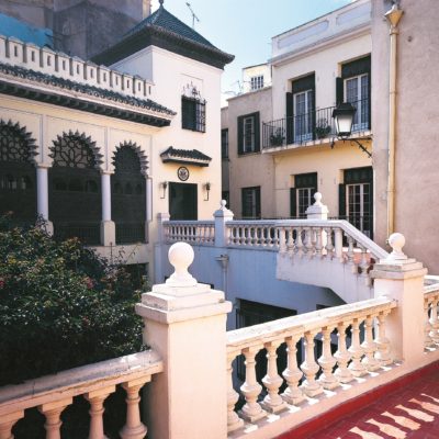 Color photograph, Color photograph, view from balcony with red tile and white balustrade with bulbous balusters across an open courtyard to a loggia. The entrance to the loggia to the side and a small, tiled hood covers the door. The seal of the United States is over the door.