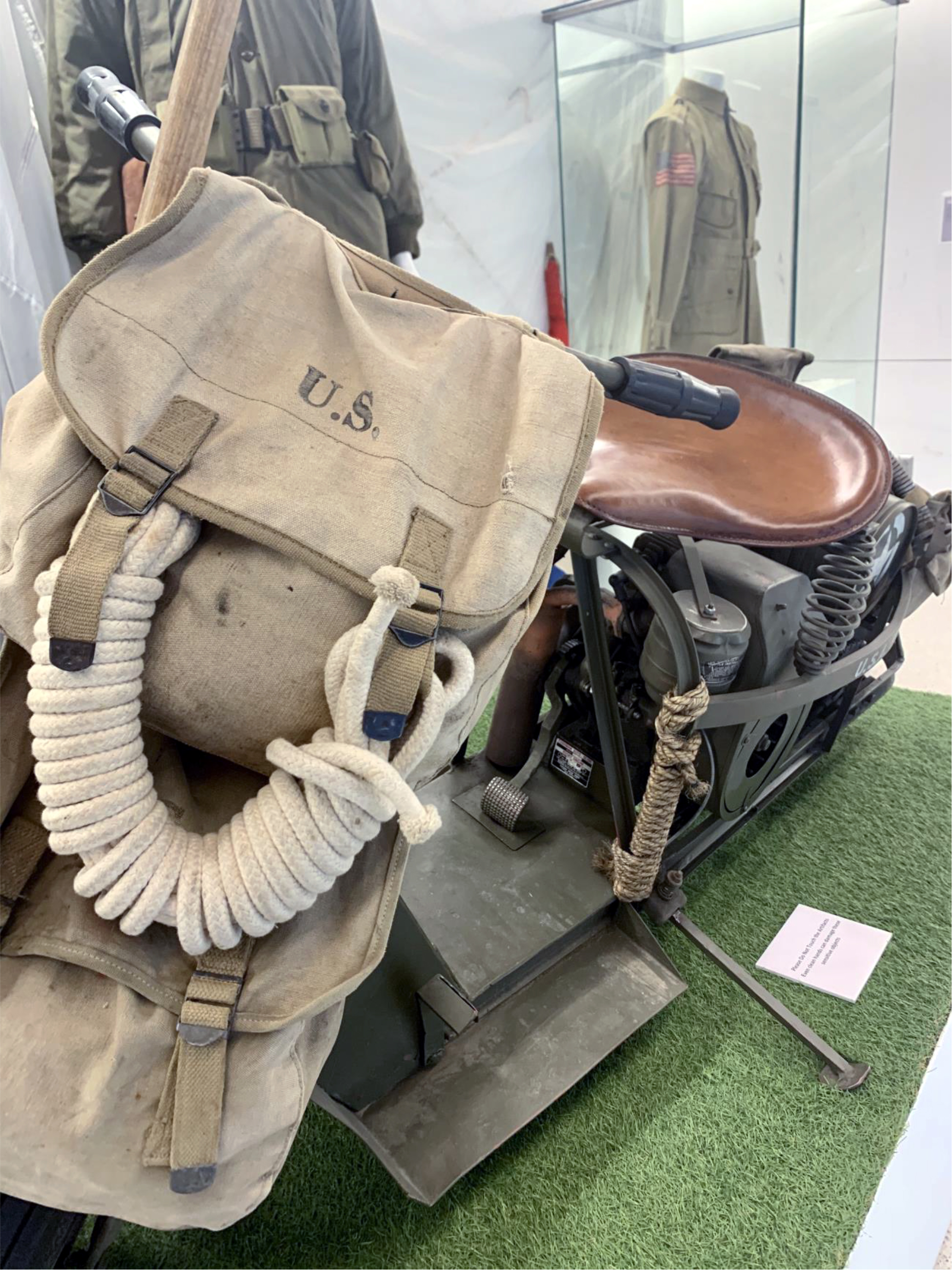 Color photograph, museum display of WWII era motorbike, U.S. Army issued backpack, and rope.