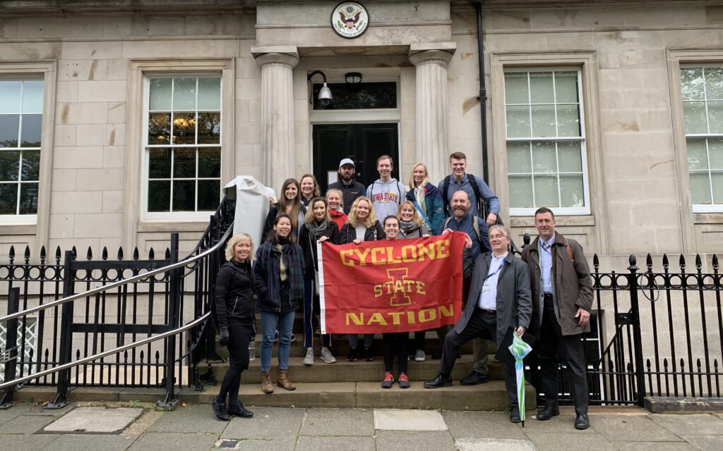 Color photograph, faculty and students standing in front of a doorway and holding a school flag.