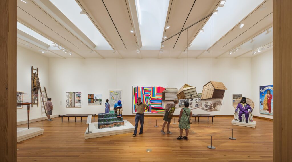 Color photograph, interior view of an art gallery with contemporary pieces on exhibit. The walls are neutral in color and the floor is made of wood.