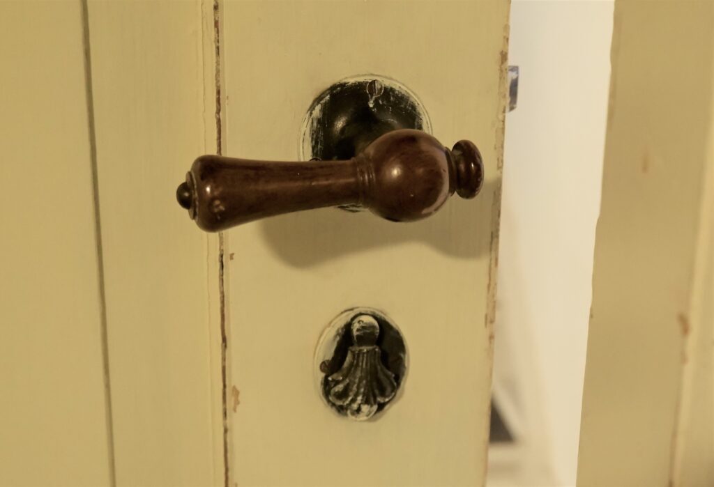 Color photograph, detail view of a wooden door that is painted to show the handle and escutcheon