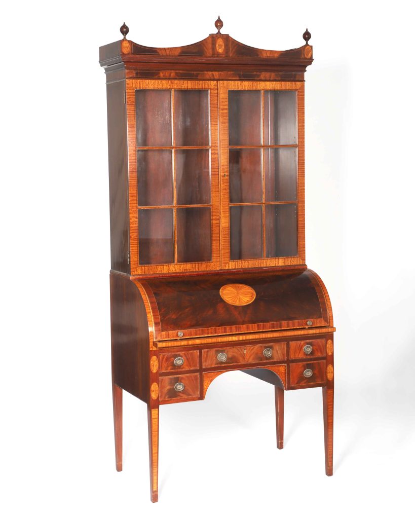 Mahogany, circa 1924-33

U.S. Embassy Lima, Peru

Schmieg & Kotzian Furniture

American, founded 1924

Founded in the 1920s, New York cabinetmaker Schmieg & Kotzian was well known for its extraordinary high-quality workmanship, producing elegant furniture in period revival styles for the U.S. Supreme Court, New York’s Waldorf Astoria Hotel, and members of New York’s social elite.

This rolltop secretary desk has both Federal and Georgian design elements and was purchased in 1950 for the newly built U.S. Ambassador’s Residence in Lima, Peru.

The Lima residence marked the beginning of a new phase in the design of U.S. diplomatic buildings. It signaled a turn away from Classical Revival architecture toward structures

based on a more contextual sensibility. The residence’s contextual design did not, however, protect it from repeated terrorist attacks in the last quarter of the 20th century. The attacks cost the lives of several local guards and damaged the house.
