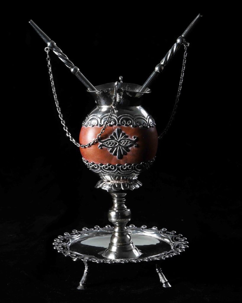 (Mate de&nbsp;Tapita, Bombilla de Plata)&nbsp;
Silver&nbsp;Mate&nbsp;cup and dried gourd with silver straws, circa 1990s&nbsp;
U.S. Embassy Buenos Aires, Argentina&nbsp;


Mate&nbsp;(rhymes with ‘okay’) in Argentina is a traditional, caffeinated herbal infusion made from dried&nbsp;yerba mate&nbsp;leaves and served communally from a shared gourd (the&nbsp;mate) with a&nbsp;bombilla, or metal straw.&nbsp;&nbsp;

The ritual of drinking and sharing tea made from hot water and&nbsp;yerba&nbsp;buena&nbsp;leaves is thousands of years old. It symbolizes friendship, hospitality and national identity and is enjoyed daily by people of all&nbsp;walks of life&nbsp;for energy and social connection. Typically, one person, (the&nbsp;cebador) prepares the&nbsp;mate&nbsp;and passes it around.&nbsp;
The silver&nbsp;mate&nbsp;features an intricately crafted eagle at its base, adding symbolic strength and elegance to its design. The couple’s&nbsp;mate&nbsp;with two&nbsp;bombillas&nbsp;is made from a dried and polished gourd, with decorative silver finishings. A couple’s&nbsp;mate&nbsp;is often given to newlyweds.&nbsp;&nbsp;&nbsp;

No record exists of the provenance of these items, but they were&nbsp;likely a&nbsp;gift, as are many items in the heritage collections of U.S. diplomatic and consular missions.&nbsp;
